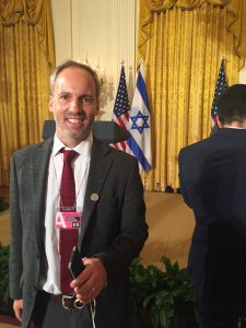 Luke stands in front of U.S. and Israeli flags at the White House.