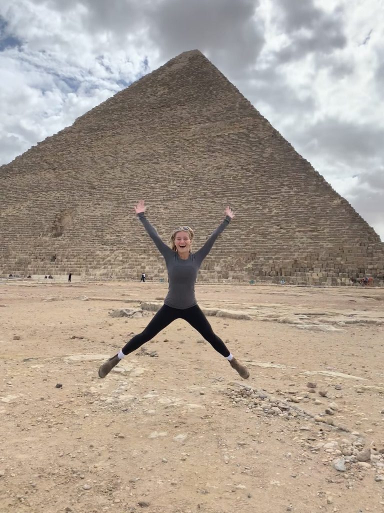 A person jumps in the air with a pyramid in the background.