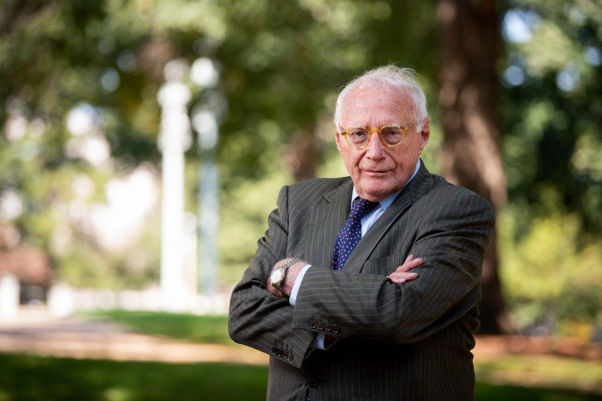 Wade Smith ’60 looks at the camera outside with his arms crossed. He is wearing a grey striped blazer.