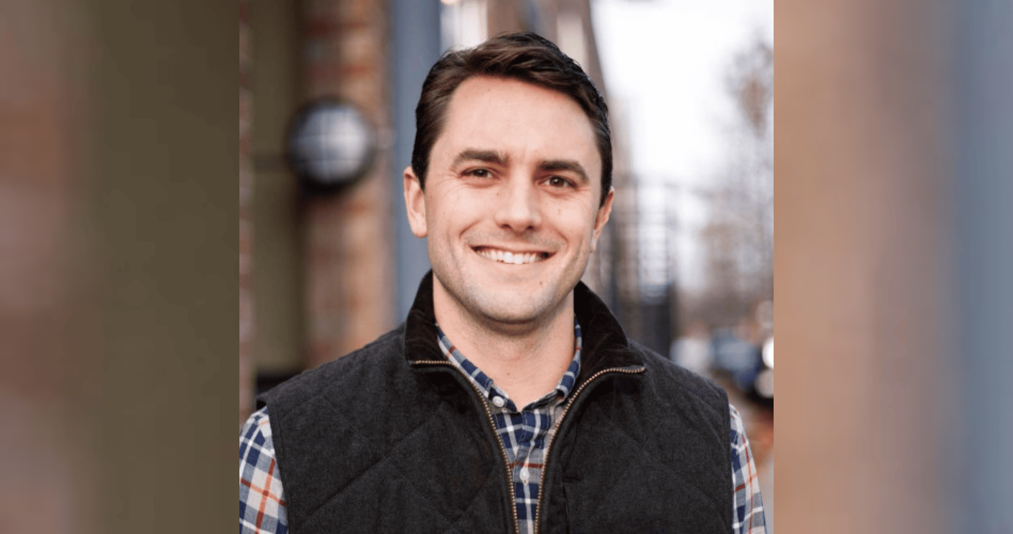 Headshot of Sebastian Williams ’11 standing in front of a street. He is wearing a black vest over a plaid shirt.