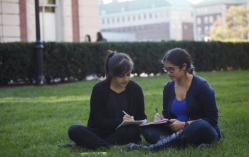 A Matriculate "Advising Fellow" mentors a student while sitting outside on the grass.