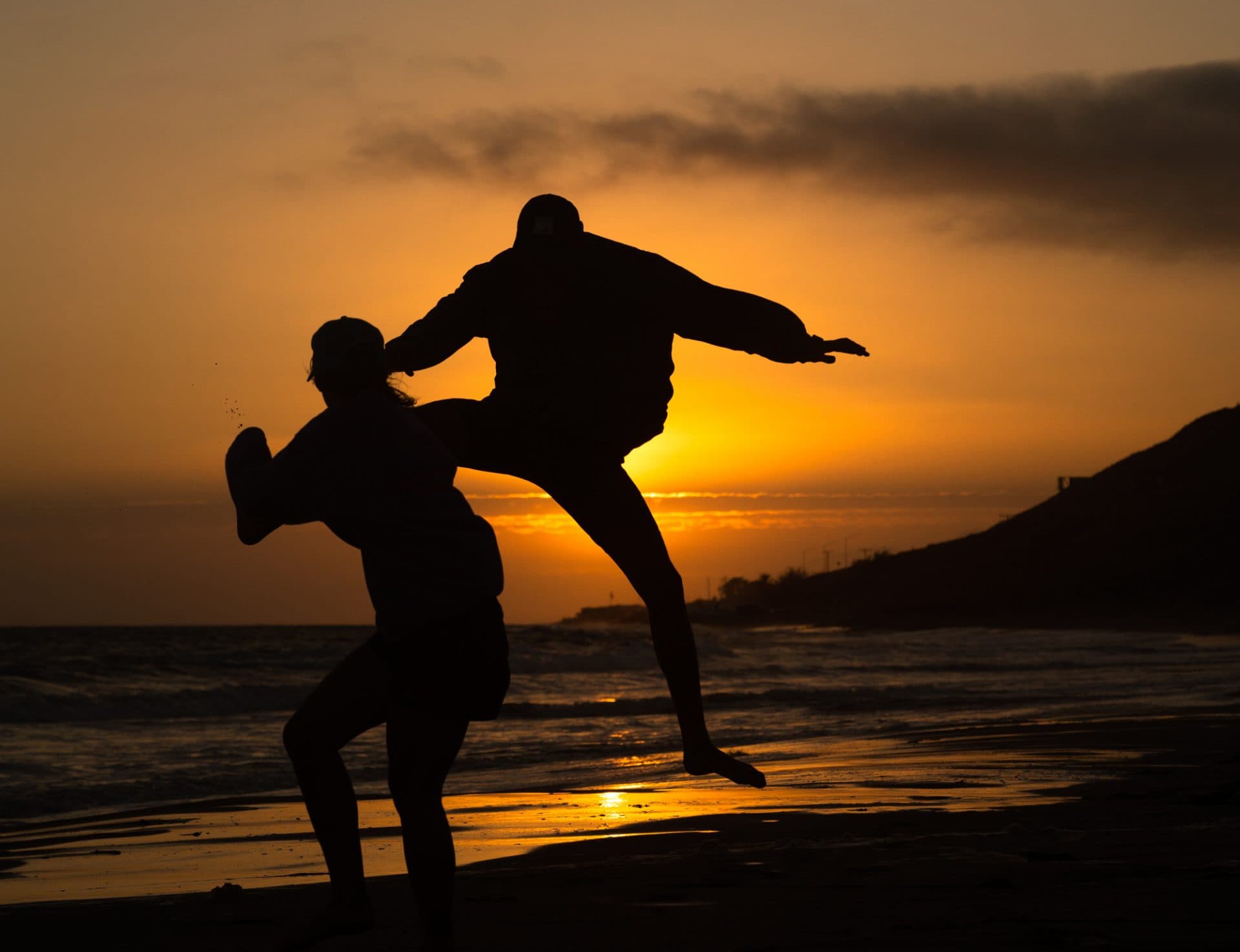 Silhouettes of two people jumping on the beach at sunset.