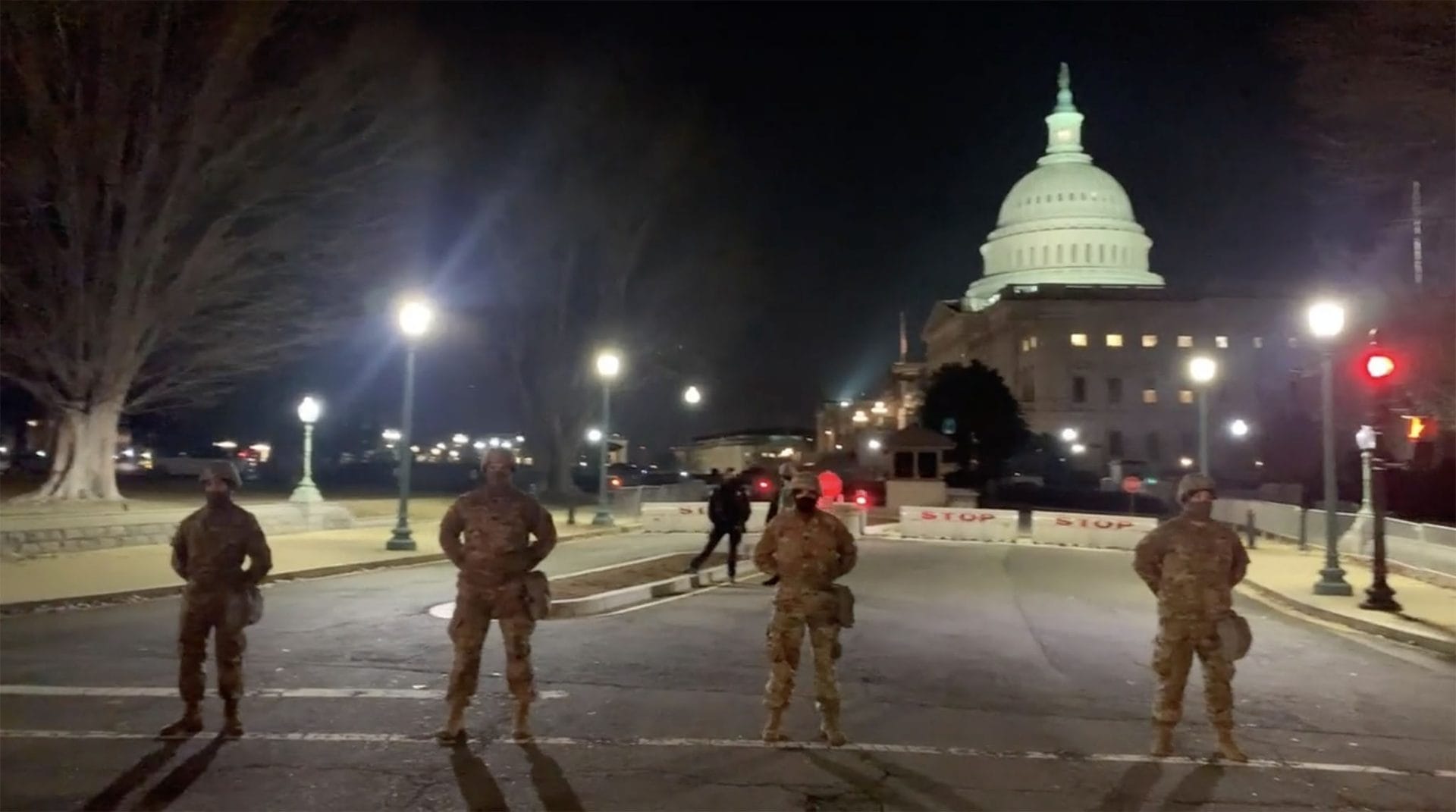 Four National Guard members stand in the road with the Capitol building in the background.