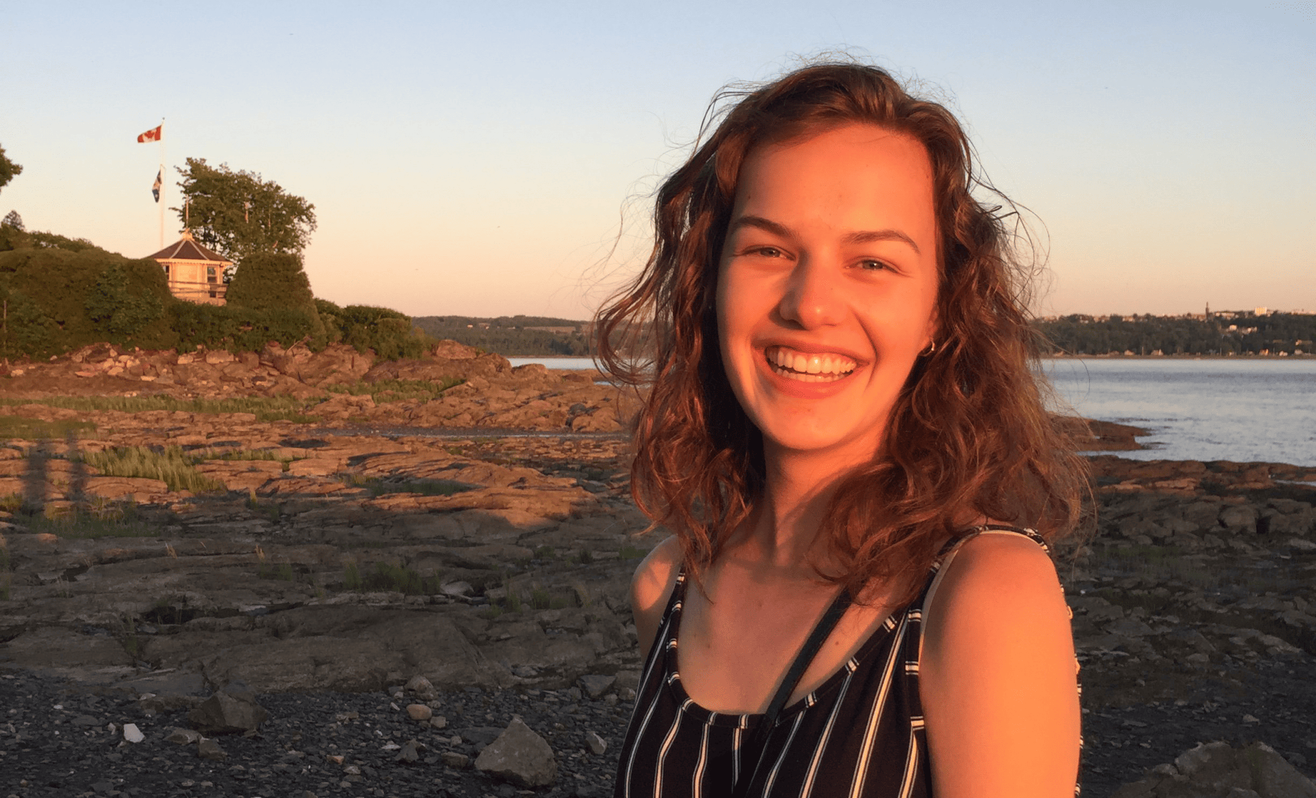 A woman smiles standing by the water at sundown.
