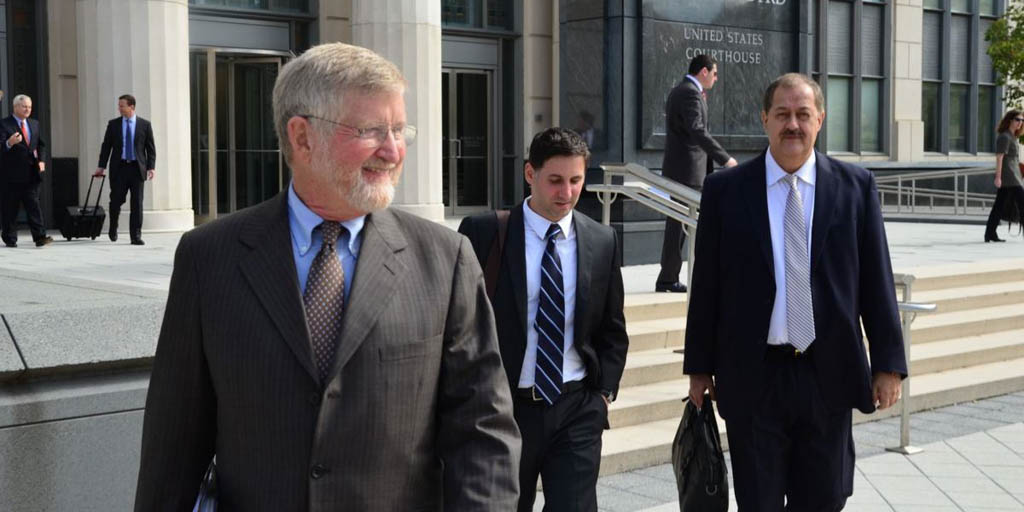 Bill Taylor ’66 smiles, looking off to his left, wearing business attire. He, along with two other men, are outside the steps of the United States Courthouse on a sunny day.