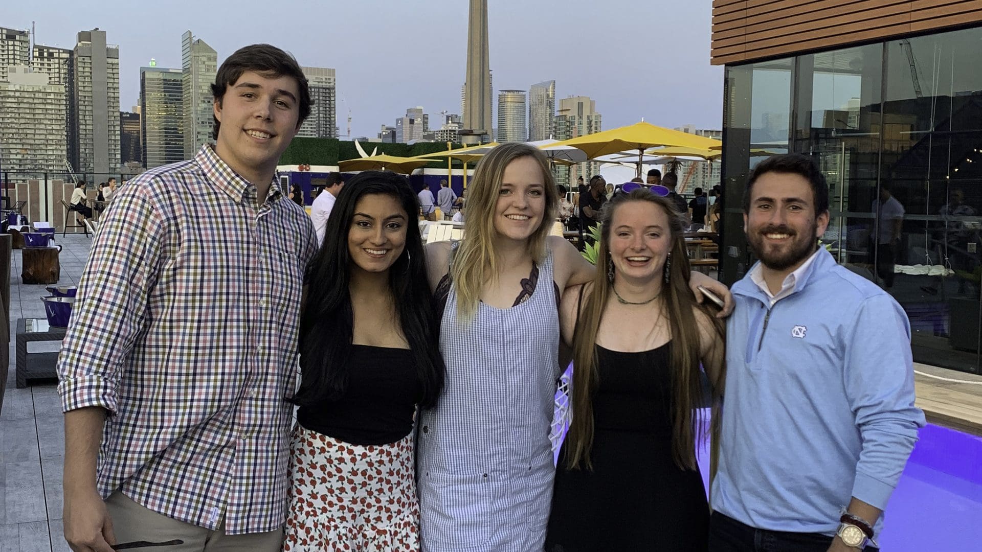 Group photo of Bobby McQueen, Jaya Mishra, Maggie Helmke, Megan Lienau, and Alex Mazer standing on the rooftop of a bar with city buildings behind her.