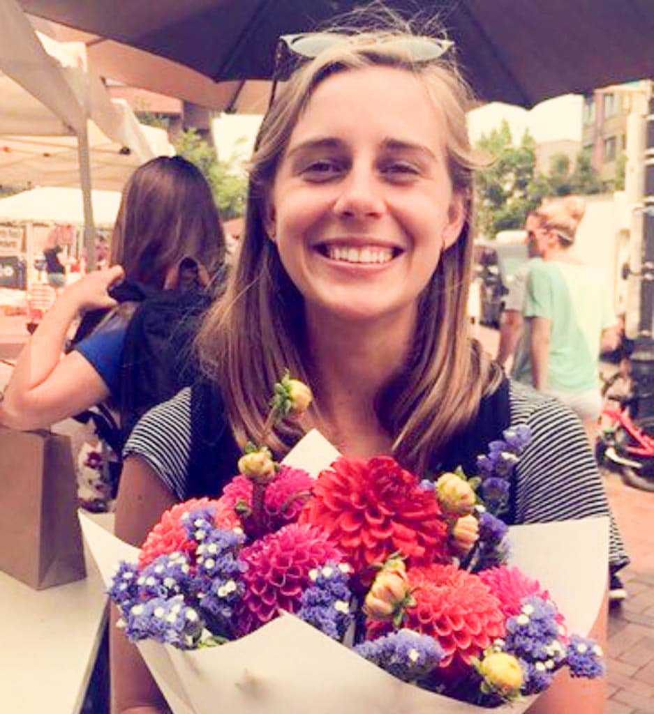 Caroline holds a bouquet of flowers at an open-air market. 
