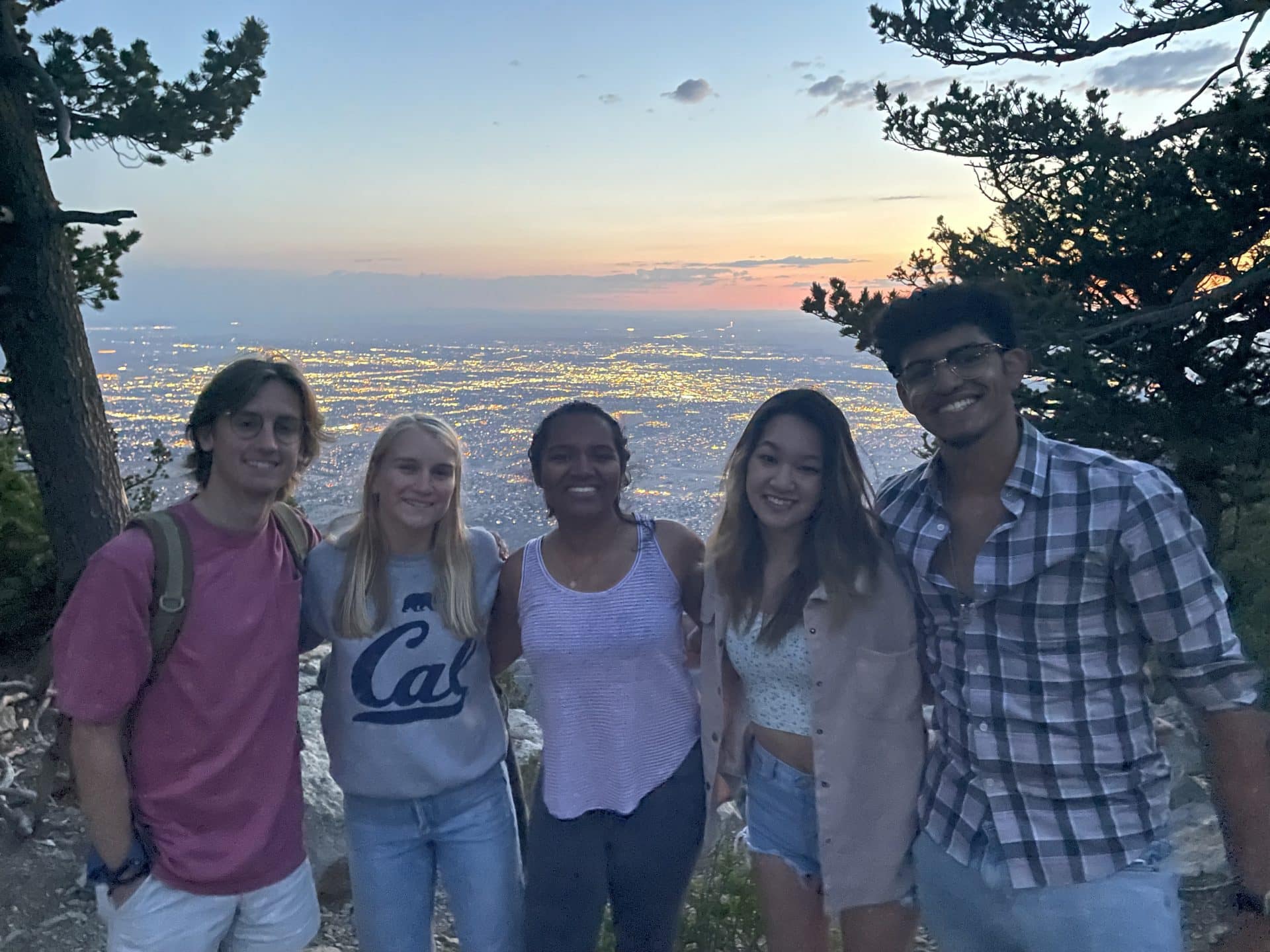 Five people smile for a photo with the cityscape and a sunset behind them.