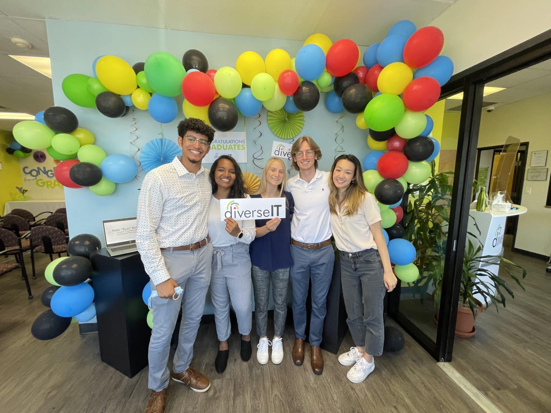 The five members of Team Albuquerque standing in front of a balloon arch and holding a sign that reads "diverseIT"