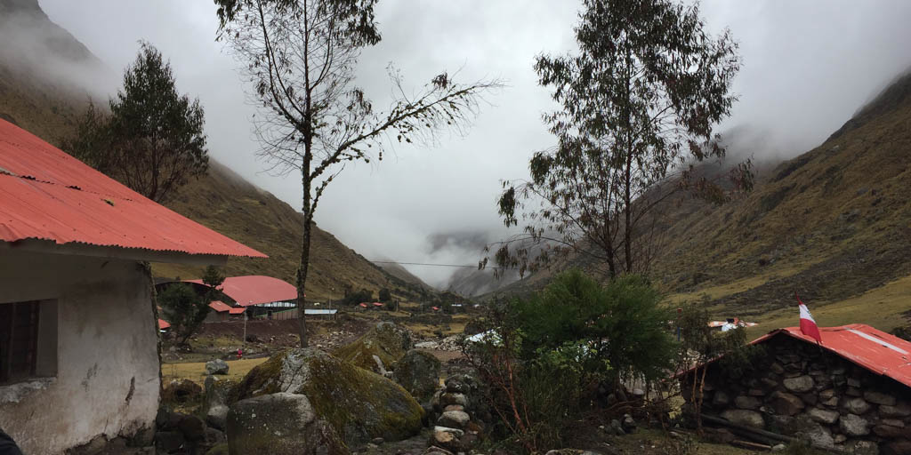 A house sits at the foothills of two mountains. There are trees and fog.