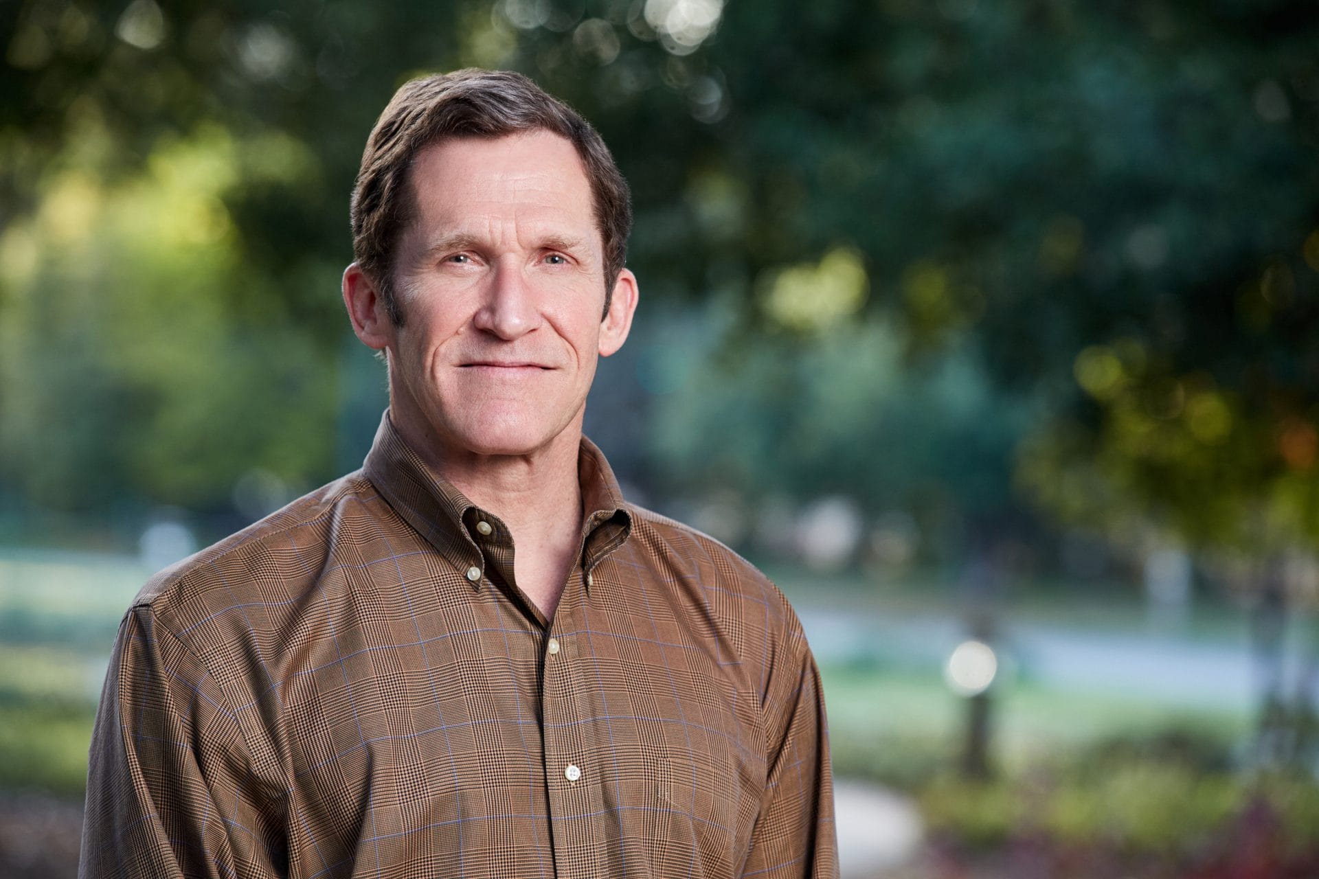 Steve Toben ’78 is wearing a brown collared shirt and looking pleasantly at the camera. Trees are blurred in the background.