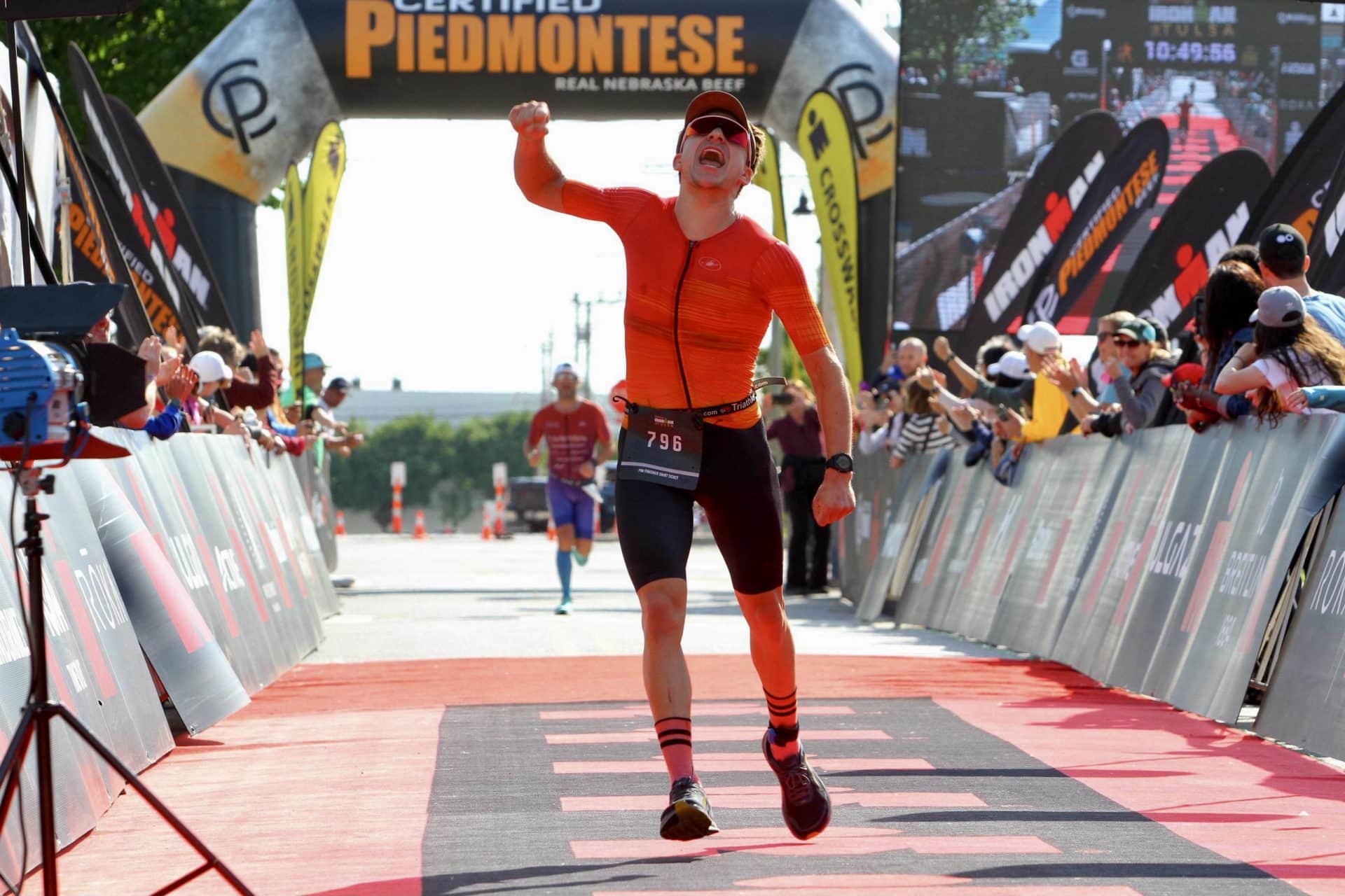 Andrew Buchanan ’23 holds a fist in the air triumphantly as he completes the race. There are supporters cheering him on each side.