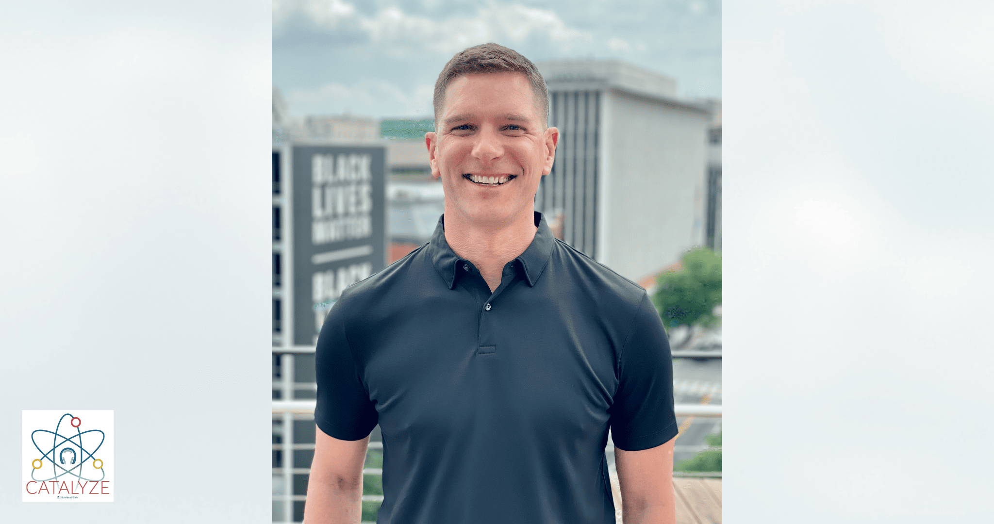 Headshot of Brad Rathgeber ’01 standing in front of some blurred buildings in the background on a sunny day. He is wearing a navy collared shirt and is smiling at the camera.