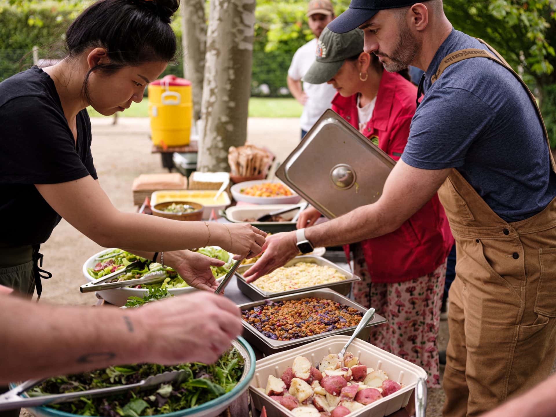 A diverse group of people standing around a table filled with delicious food.