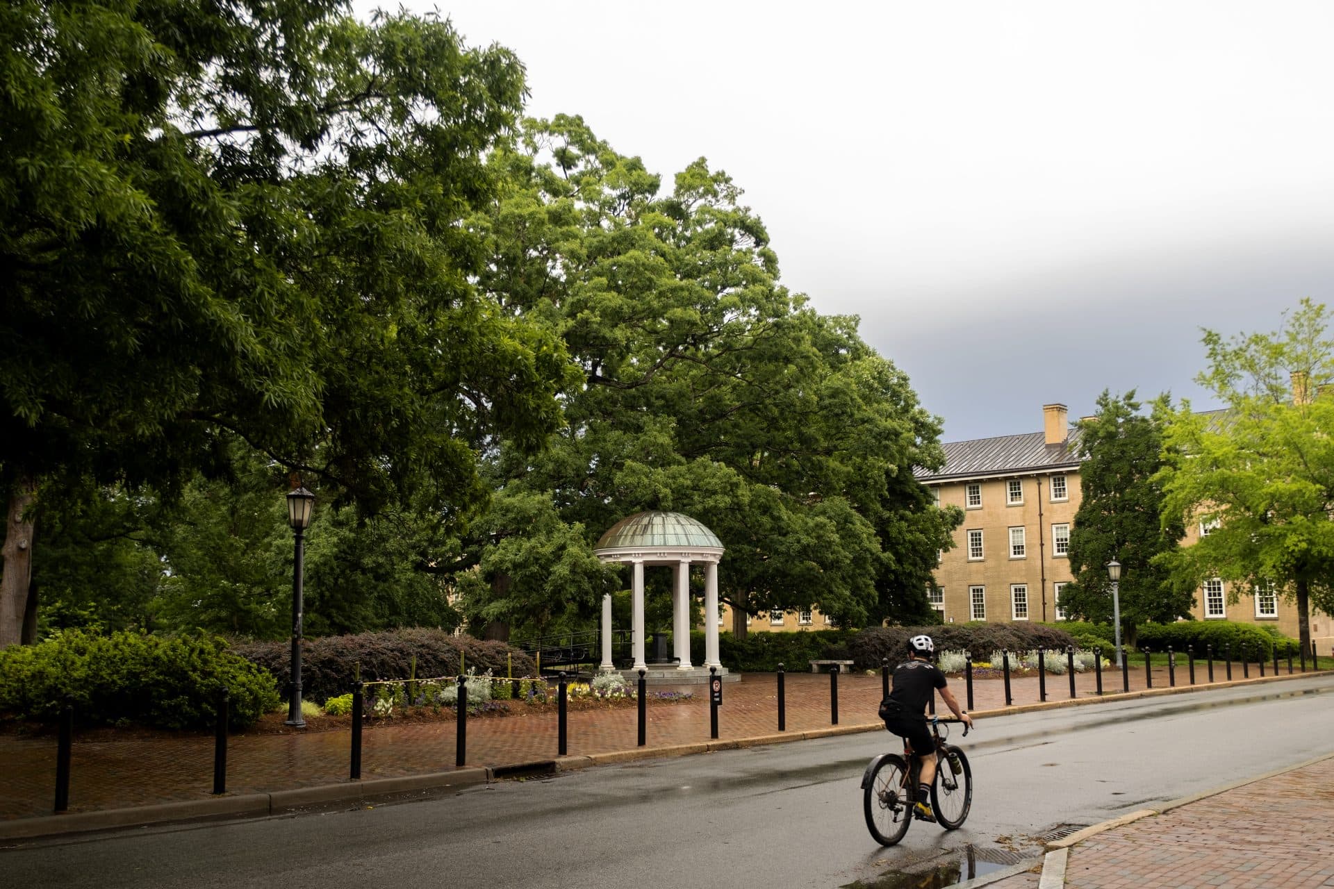 A bicyclist rides past the Old Well on a rainy day.