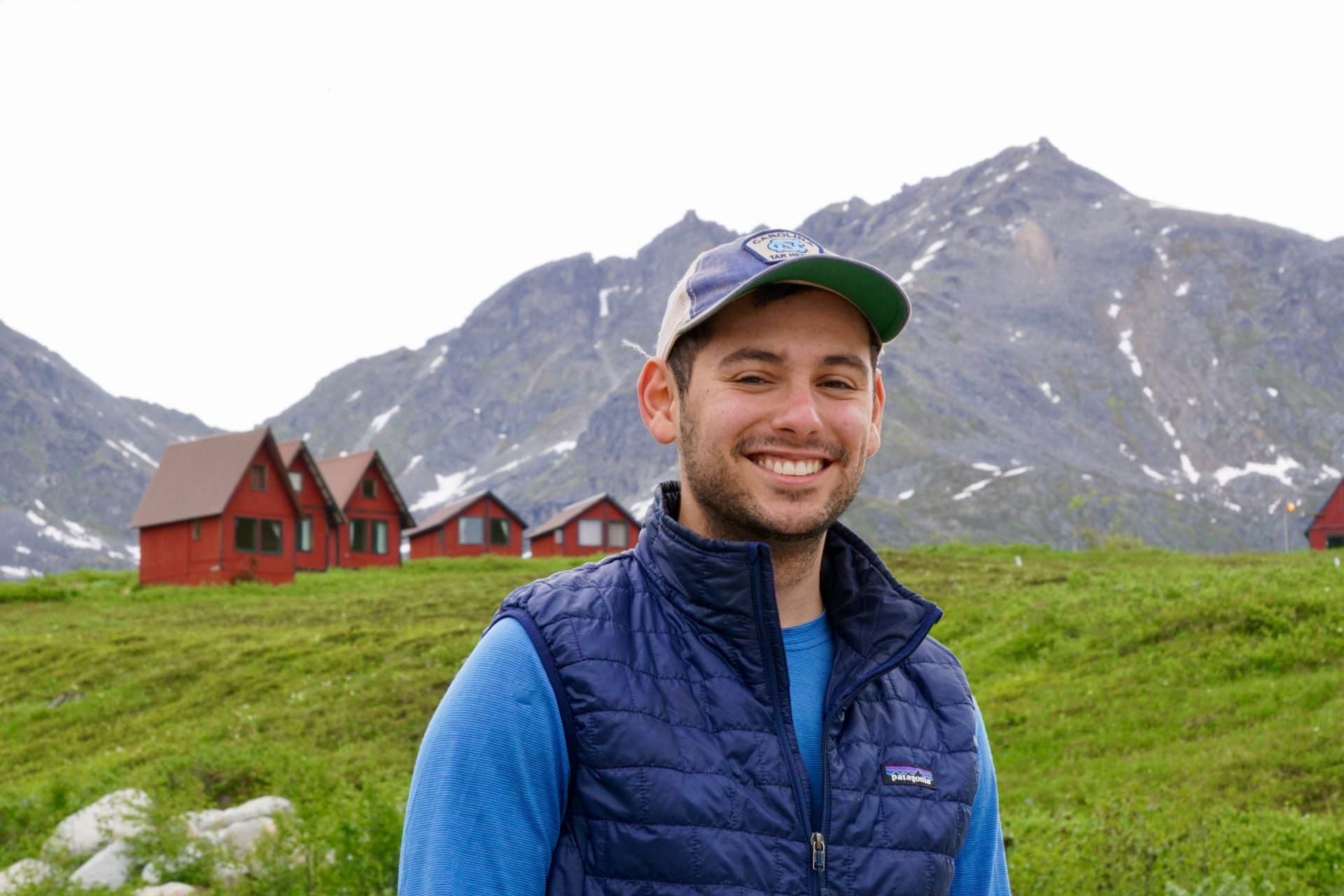 Evan stands in front of mountains and small red houses. 