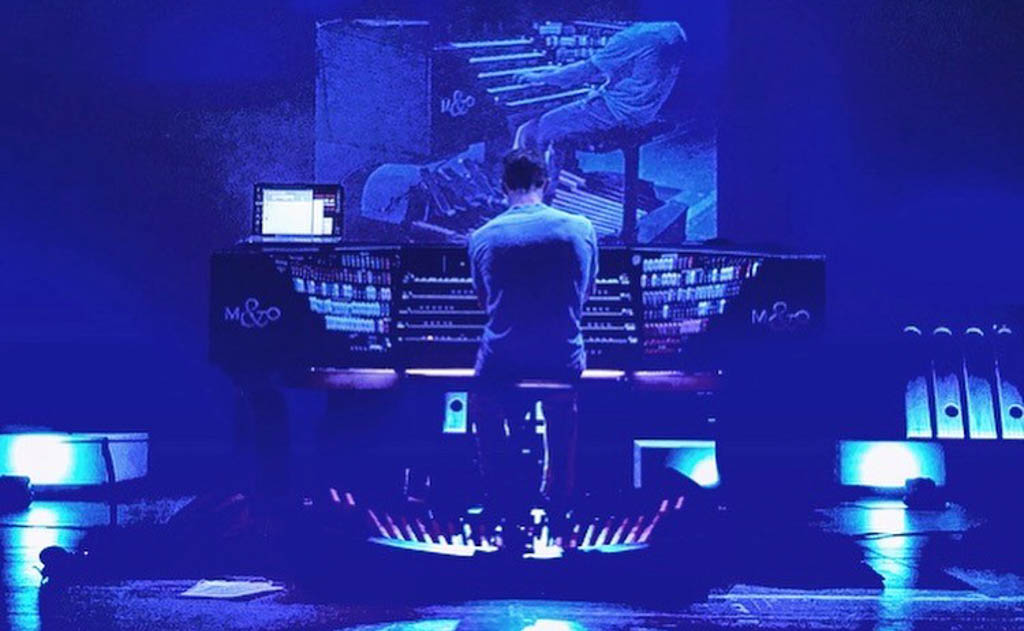 Jacob plays an organ, with his back turned to the audience, onstage.
