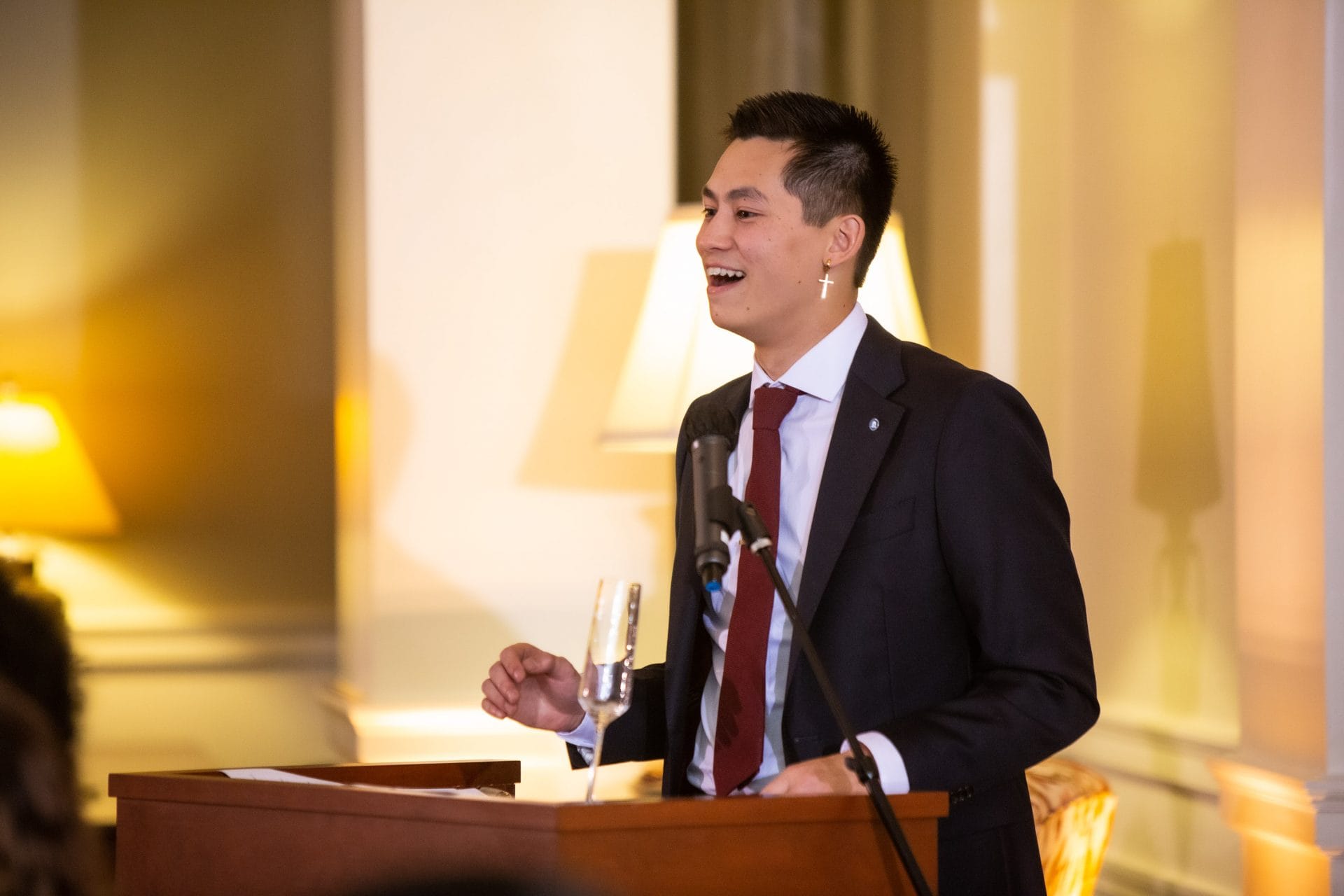 Tai Huynh in a suit standing behind a podium delivering a speech.