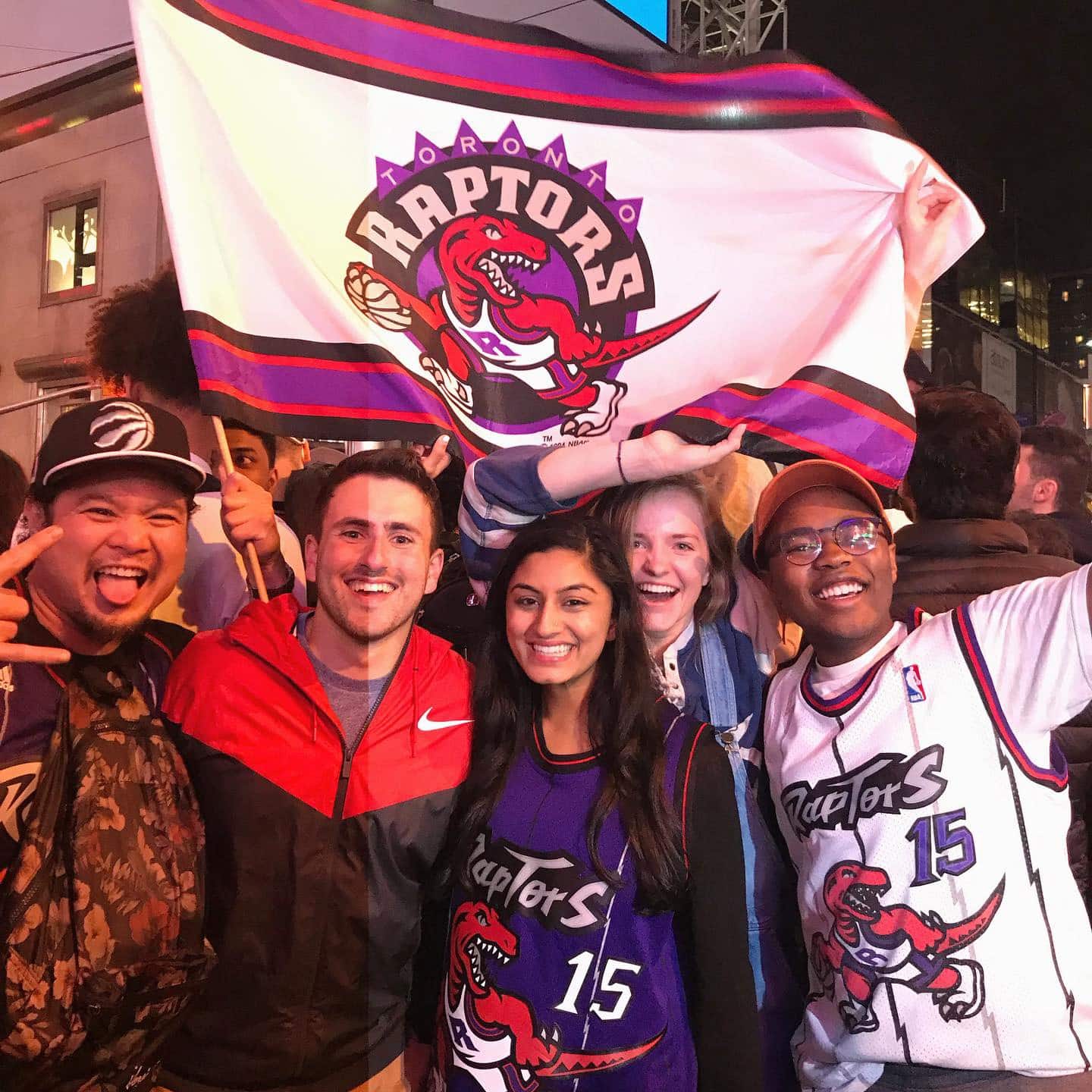 A group of five people smile for the camera holding a Toronto Raptors flag after the championship game.