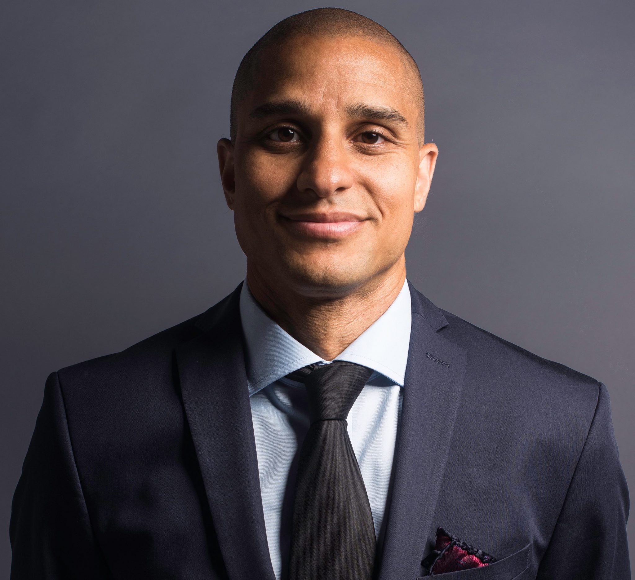 Headshot of Brian Strong ’00 wearing a navy blazer and black tie.