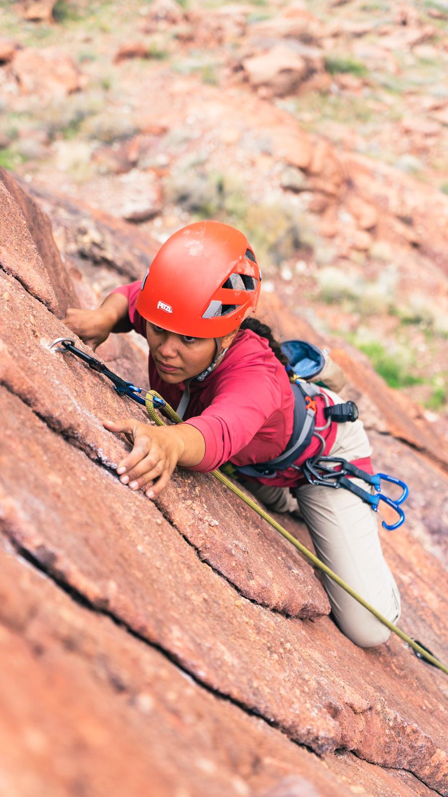 A woman in a red helmet scaling a rock formation.