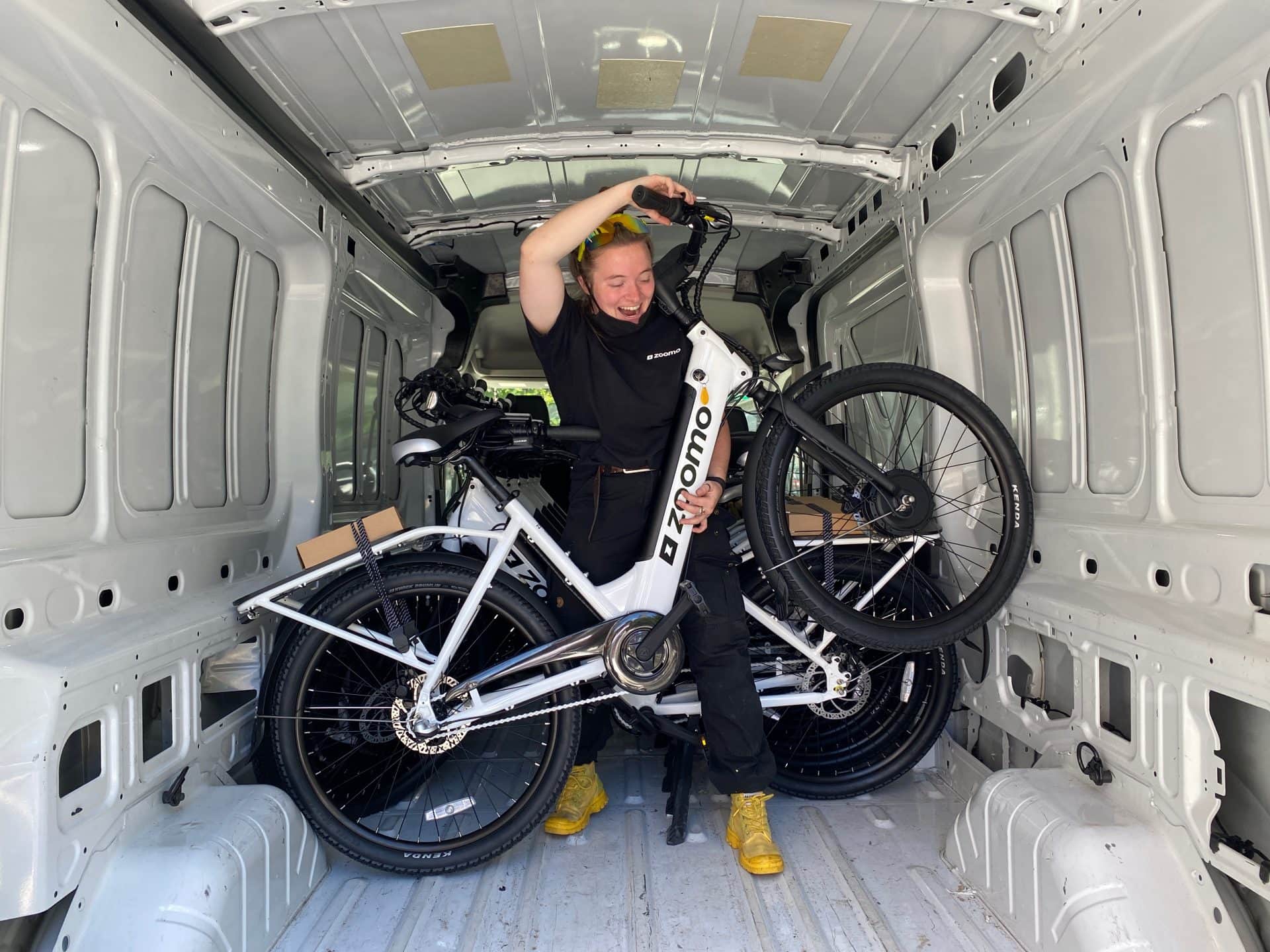 Megan holds up a Zoomo bike inside of a large supplies van.
