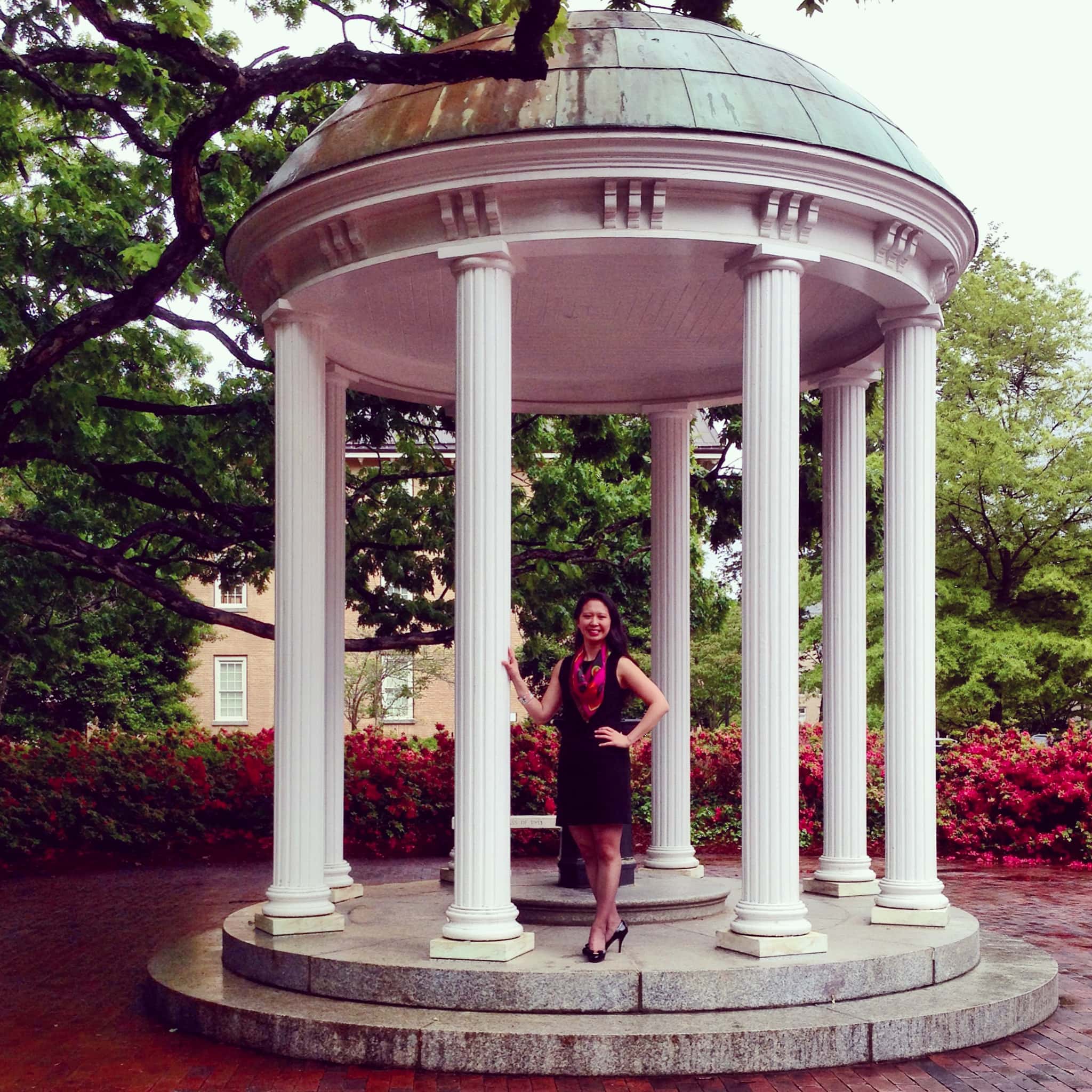 Angela Liu ’04 stands with a hand on one of the pillars at the Old Well on a rainy spring day.