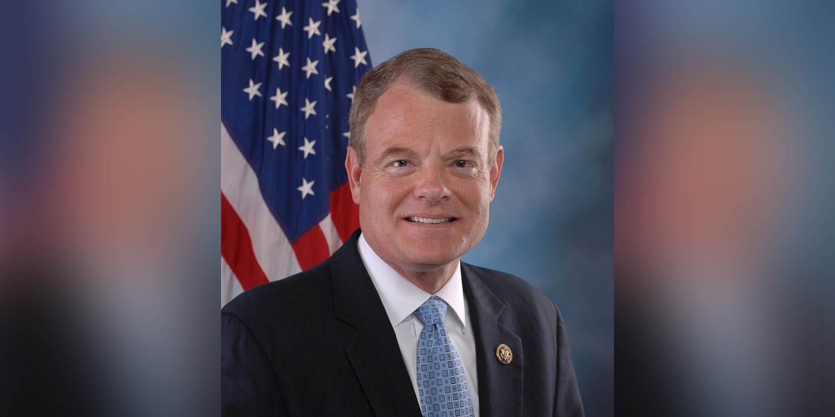 Mike McIntyre in a suit smiling in front of the American flag.