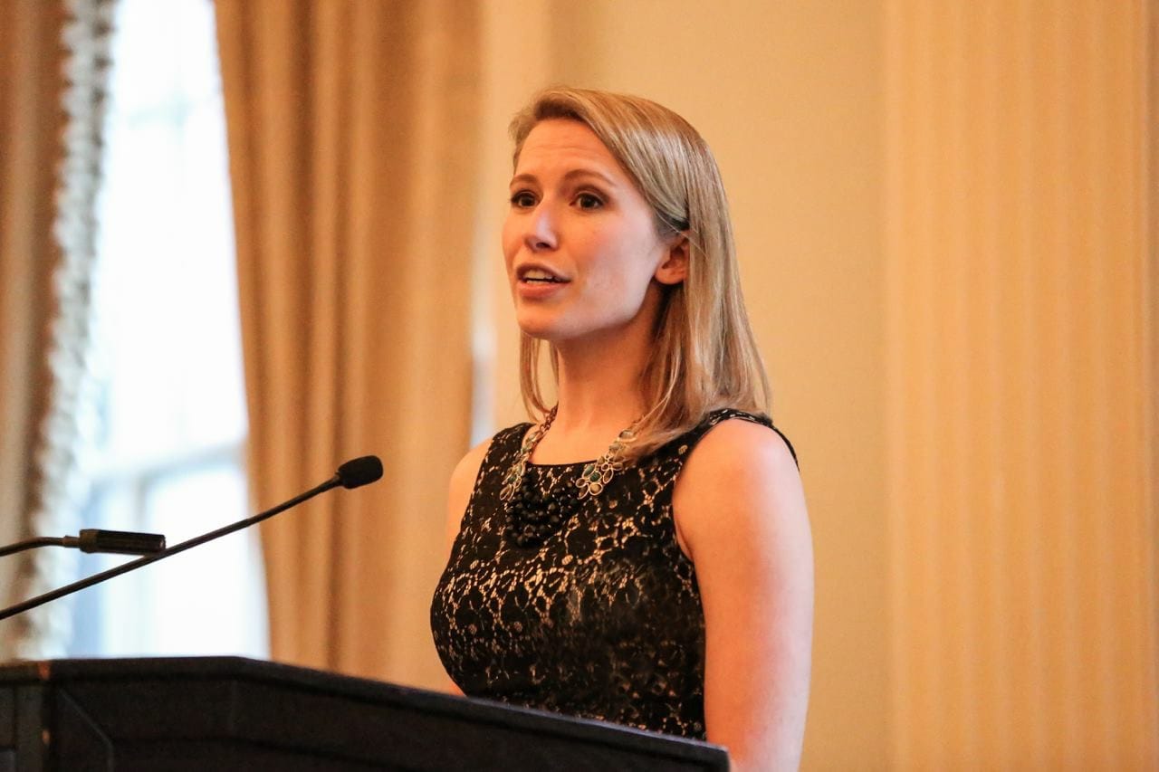 Hadley speaking into a microphone at a podium.