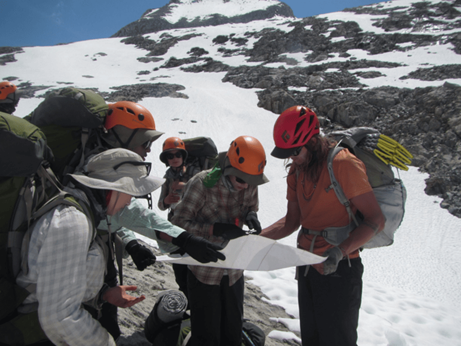 Hikers study a map together on a snowy mountain.