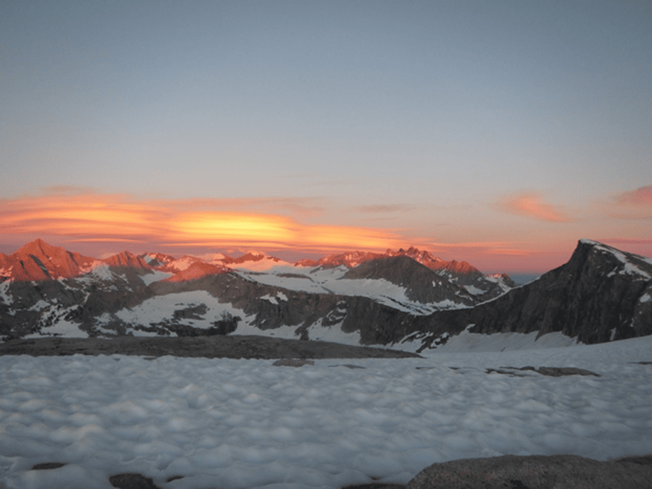 A sun sets behind a snowy mountain.