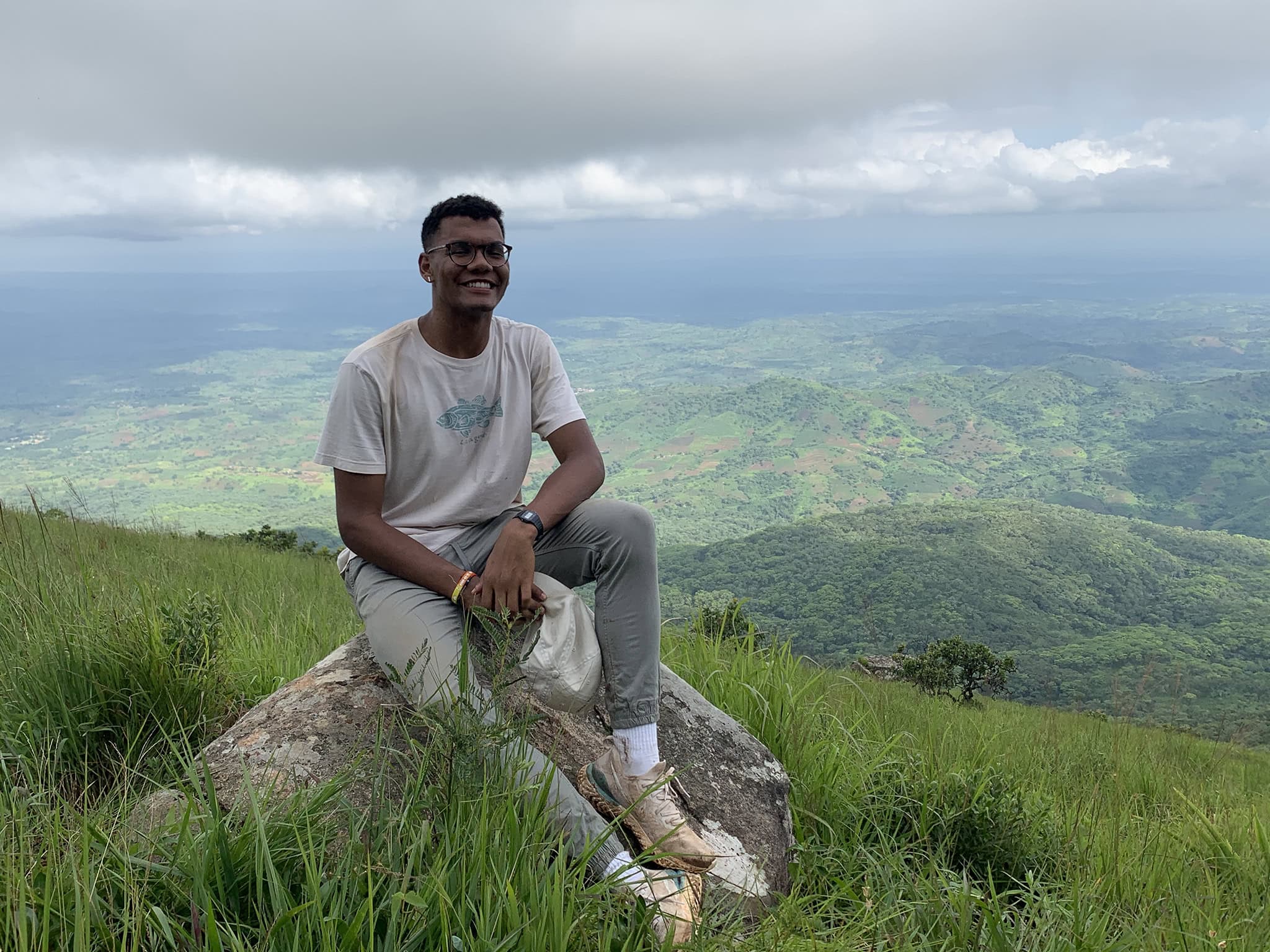 Emile Charles ’24 sits on a boulder atop a grassy mountain in Malawi.