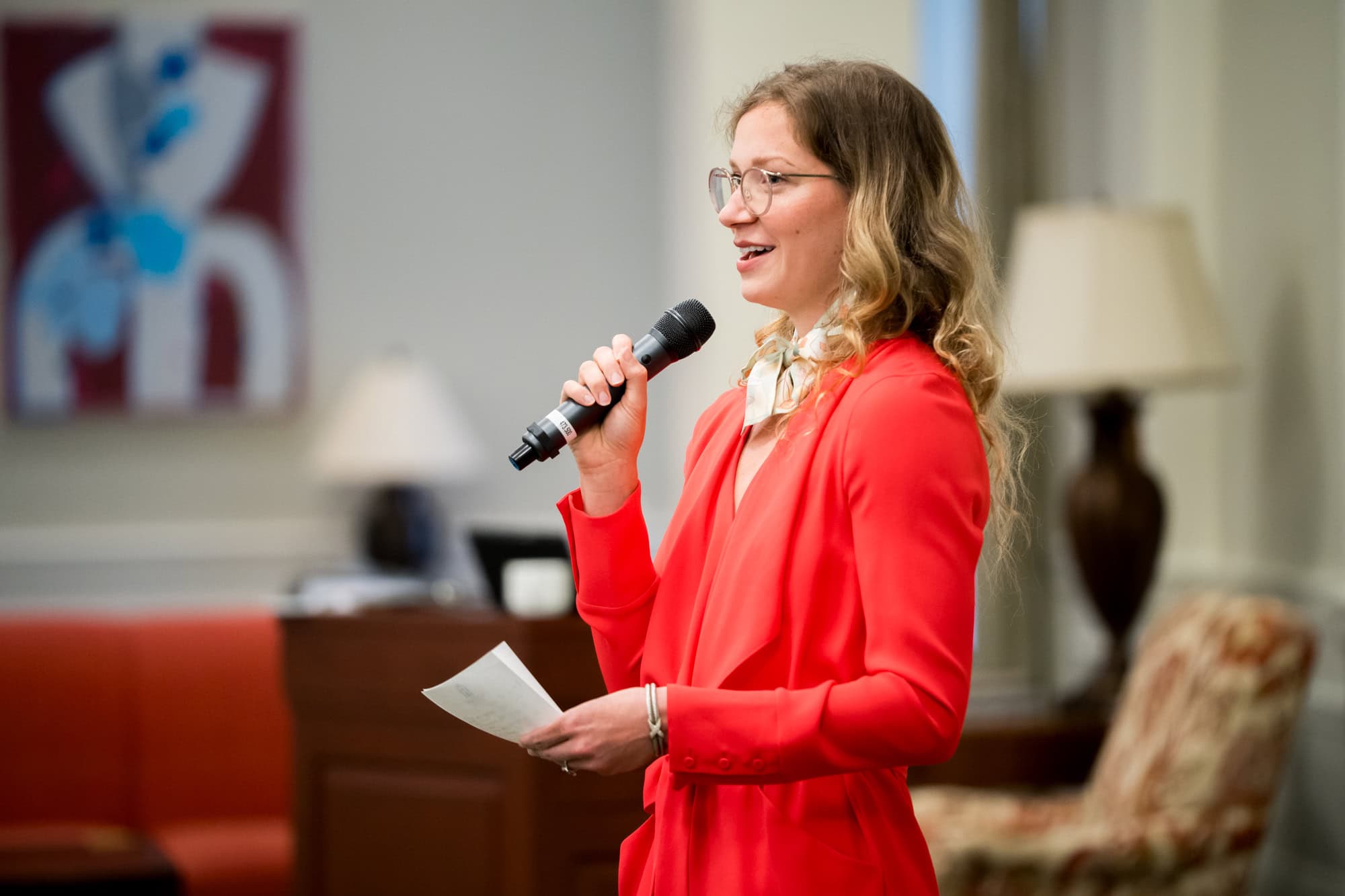 A woman wearing business attire speaks into a mic at an event for students.