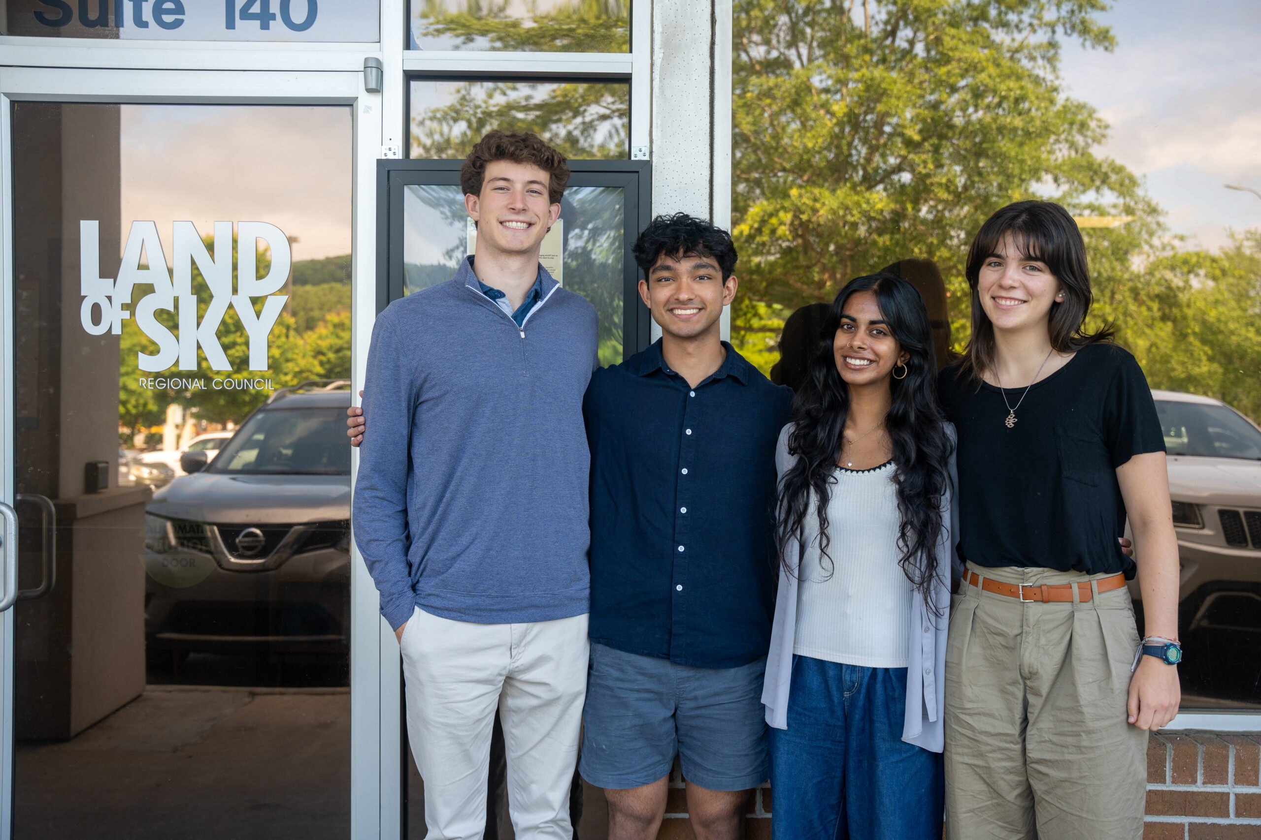 Four college students smile outside the Land of Sky Regional Council office building