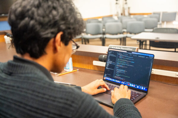 Student types on a laptop screen of code