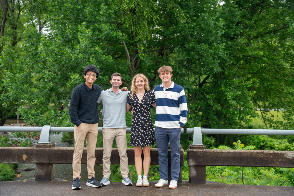 Four college students pose together in Black Mountain, North Carolina, on a bridge overlooking a river.