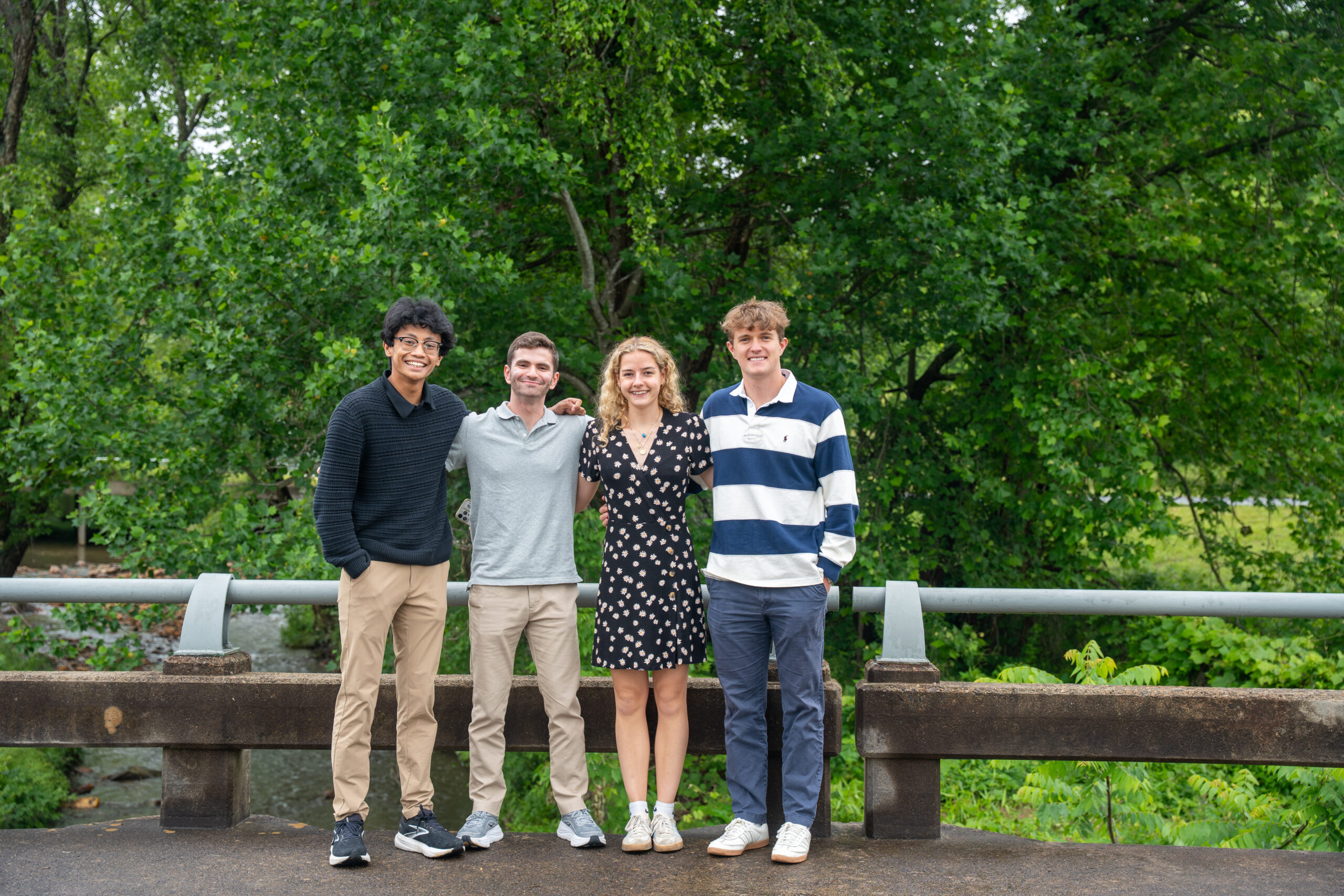 Four college students pose together in Black Mountain, North Carolina, on a bridge overlooking a river.