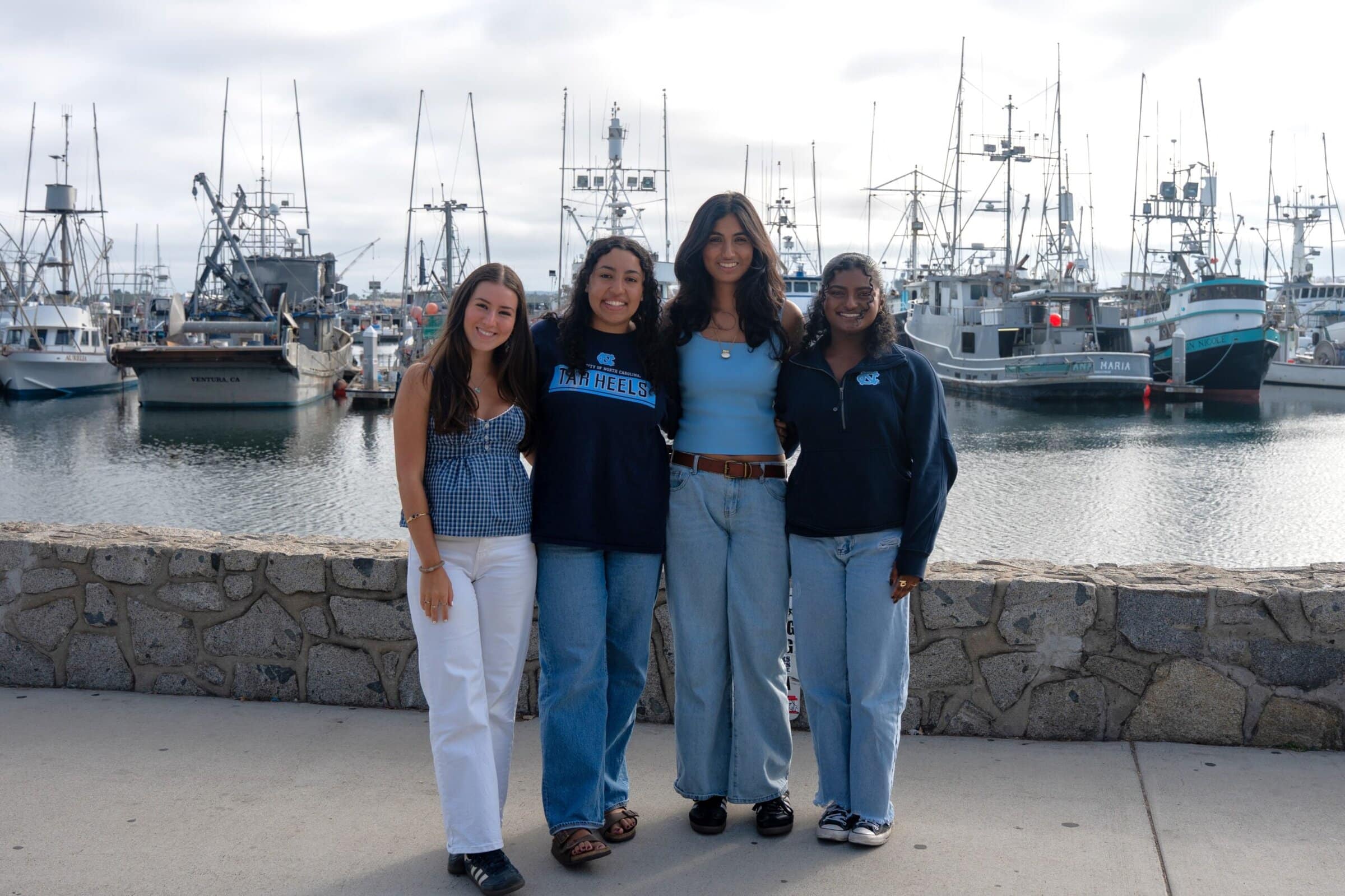 Four students stand smiling in front of a marina of boats in the San Diego Harbour.