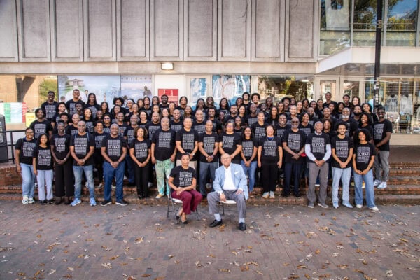 Large group standing outdoors posing for camera with 50 years of black excellence t shirts 