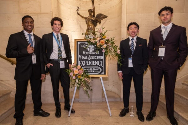 Four males smile by Final Selection Experience chalk sign
