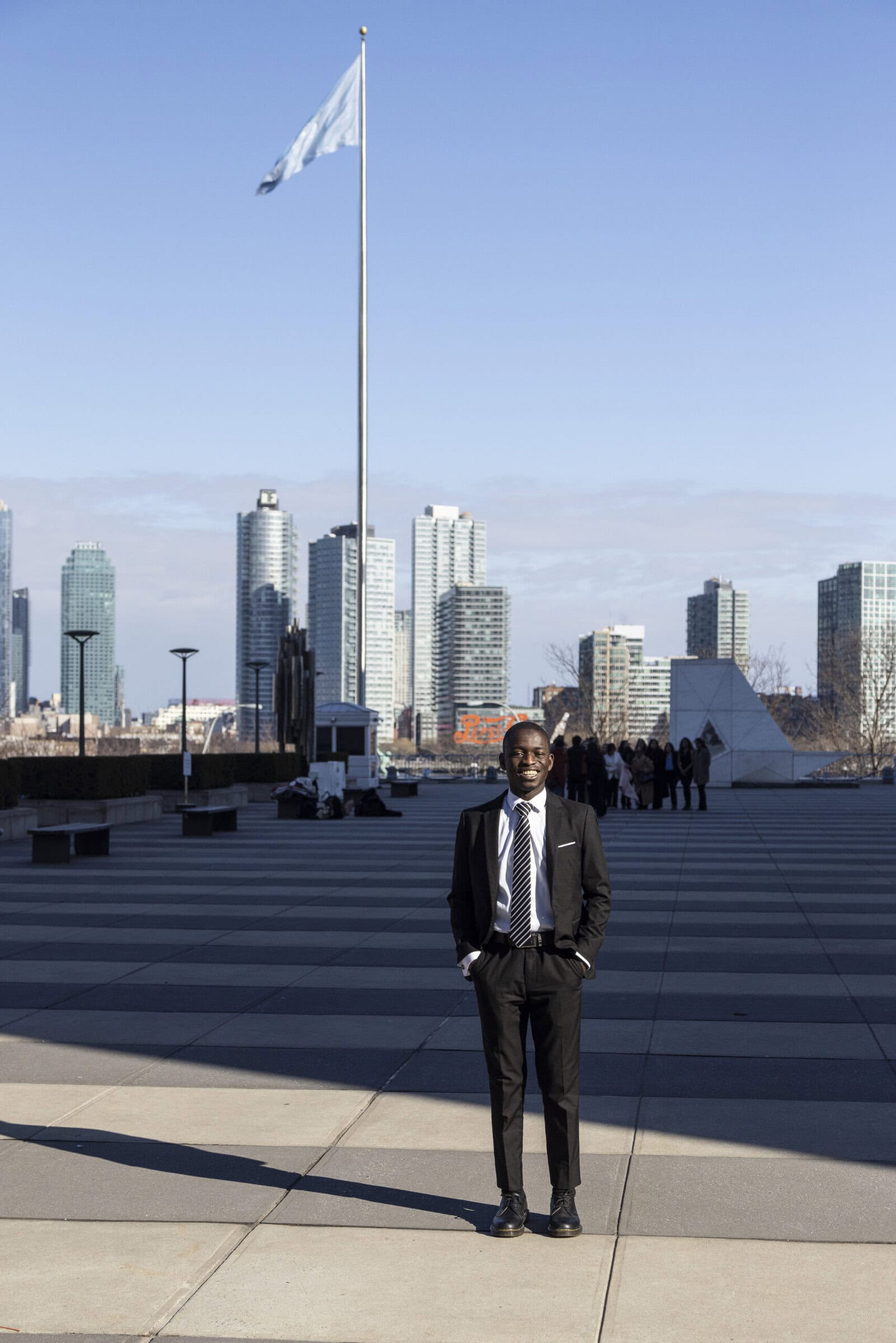 A student in business attire stands outside the United Nations on a sunny day in New York City with buildings in the background.