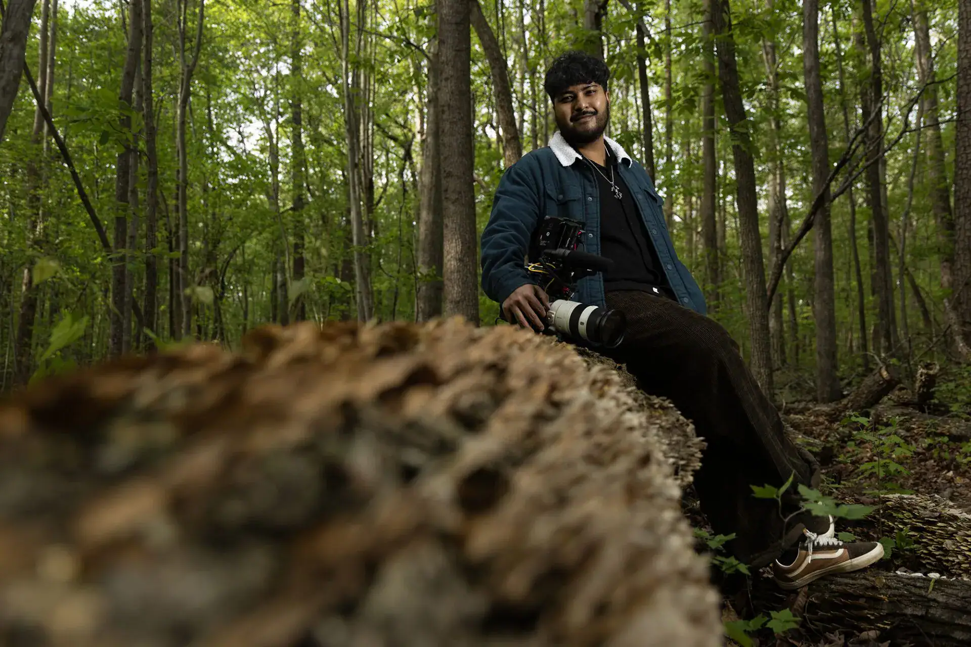 Aayas Joshi sits with his camera on a log in the woods