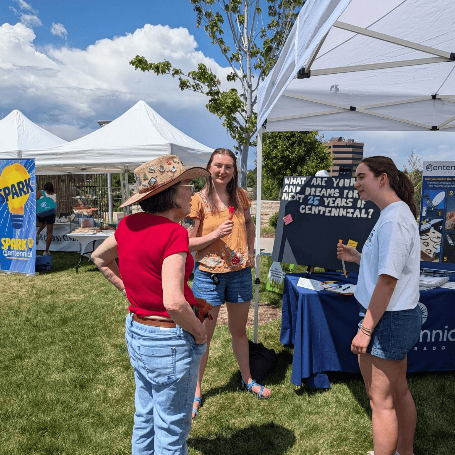 Two students speak to a resident at an outdoor community event under tents.