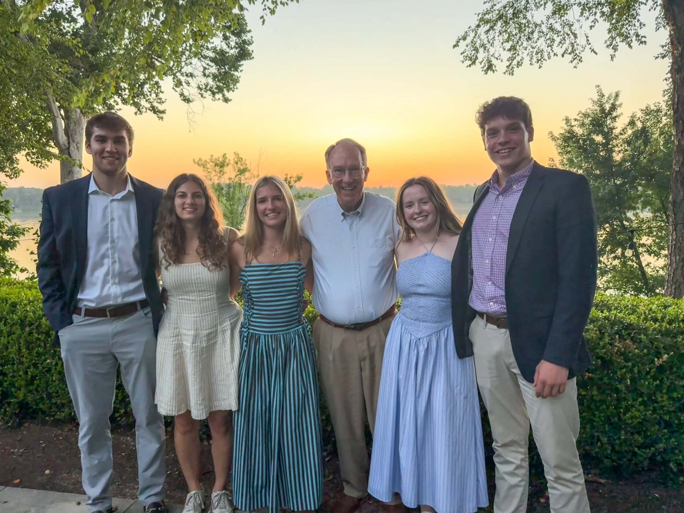 Five Morehead-Cain scholars stand with Prospect Mayor Doug Farnsley ’73 outdoors at sunset, with trees and a scenic landscape in the background.