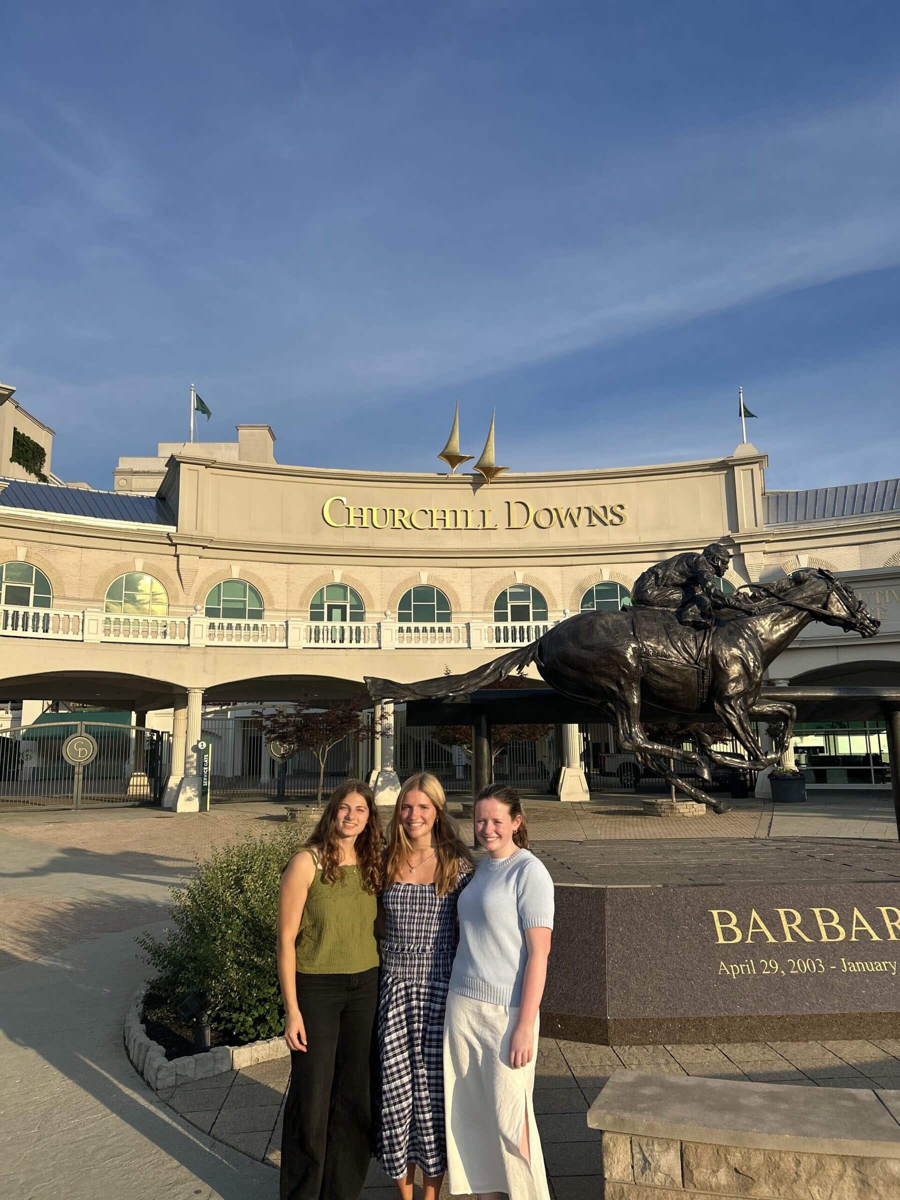 Three Civic Collaboration team members pose in front of the Churchill Downs entrance and a statue of a jockey riding a horse in Louisville, Kentucky.