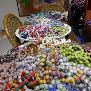 Colorful textile necklaces are arranged on white trays and tables indoors.