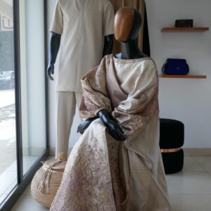 Two mannequins display light-colored garments inside a bright fashion boutique, with woven baskets and accessories nearby.