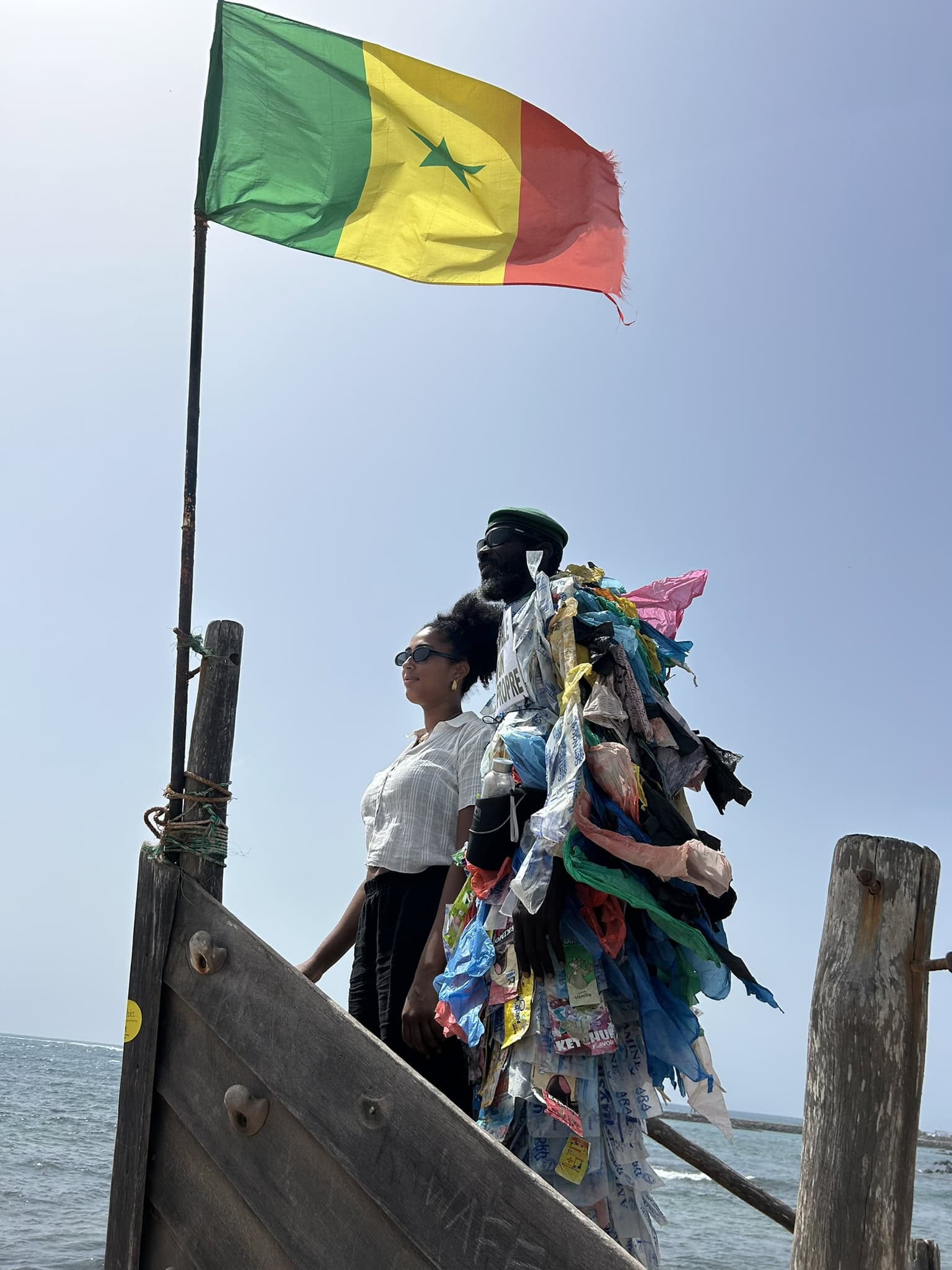 Anjali stands beside environmental activist Modou Fall, who wears clothing made from discarded plastic, near the shoreline at Pointe des Almadies in Senegal.
