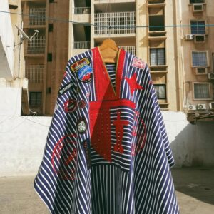 A striped blue-and-white garment with red appliquéd designs hangs outdoors between apartment buildings.