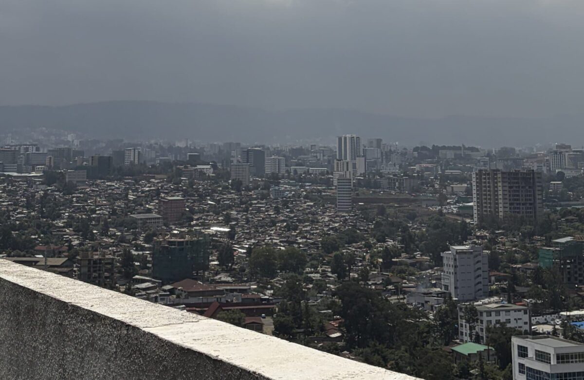 Addis Ababa stretches across a valley beneath heavy clouds, with neighborhoods, high-rise buildings and mountains visible in the distance.